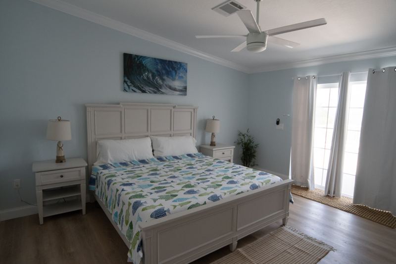 King bed in a master suite with ocean artwork and a ceiling fan