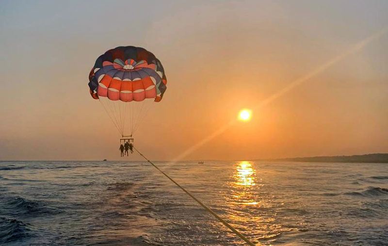 Three people parasailing over the water at sunset